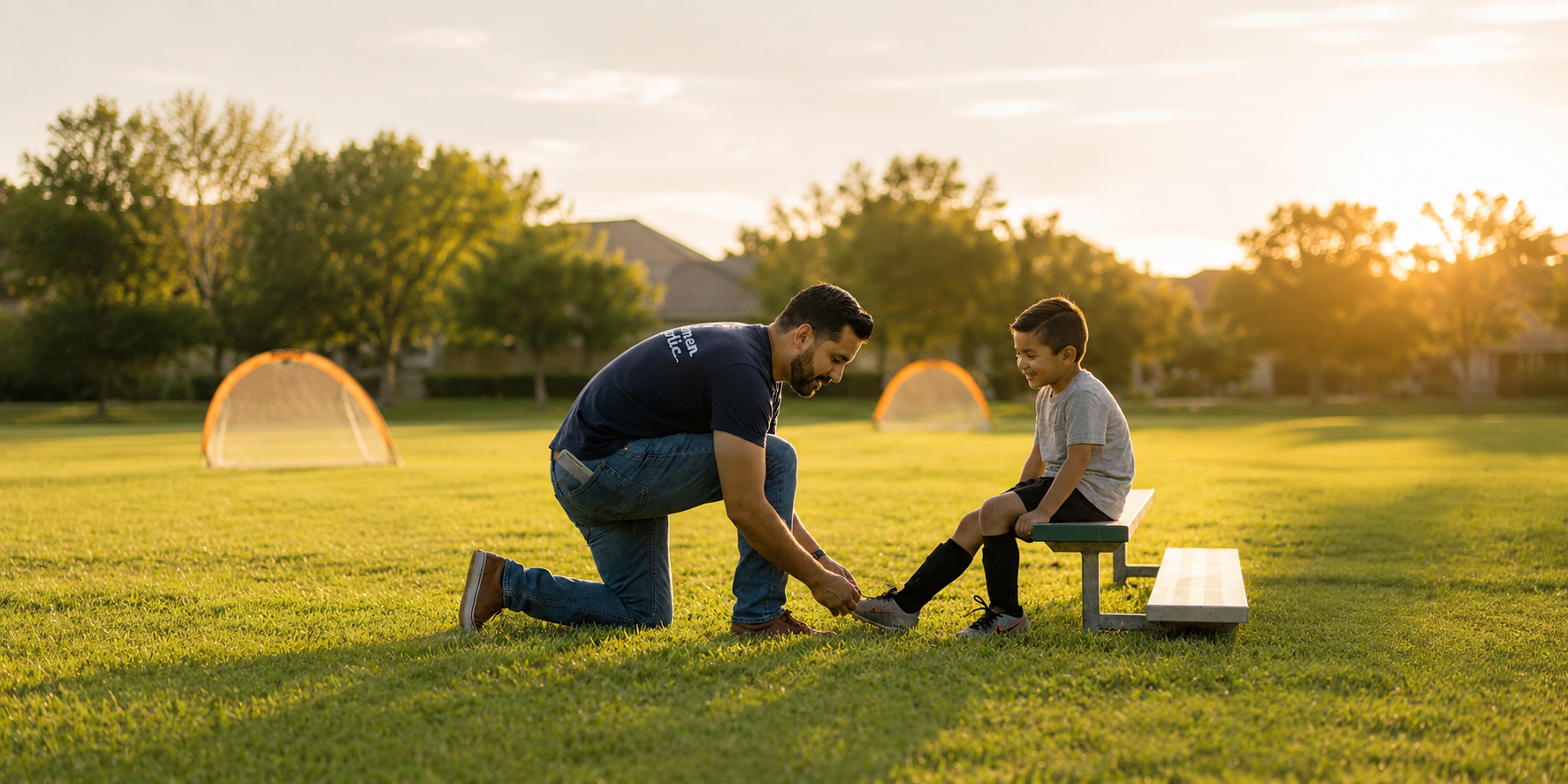 Man and child playing with a kite on a grassy field at sunset